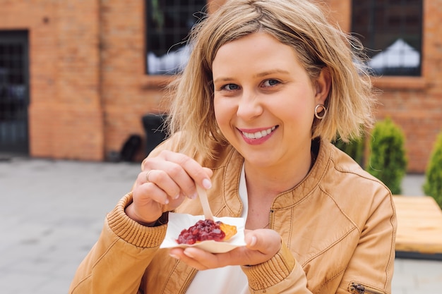 Zdjęcie uśmiechnięta młoda kobieta patrzy na aparat i holdplate smażony ser z dżemem jagodowym w ręku. smak i przyjemność. podróż i turystyka. styl życia. świetnie się bawimy. tradycyjna kuchnia narodowa.