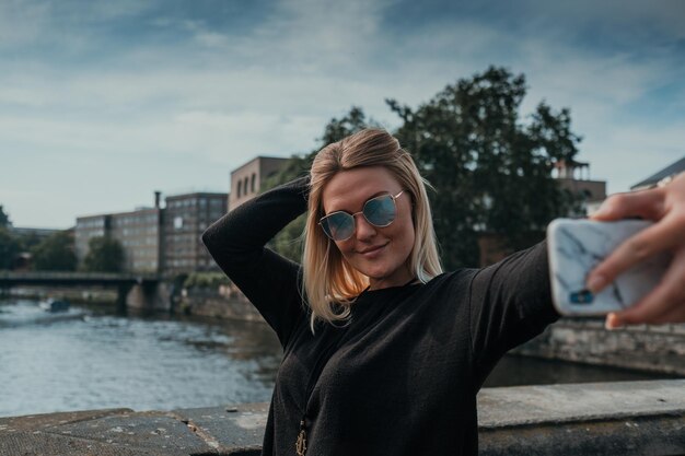 Uśmiechnięta młoda kobieta robiąca sobie selfie stojąc w mieście