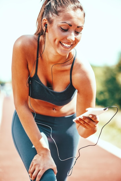 Uśmiechnięta młoda kobieta słucha muzyki na słuchawkach i odpoczywa po joggingu.
