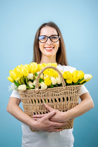 Uśmiechnięta młoda kobieta trzymająca żółte tulipany w koszu na niebieskim tle