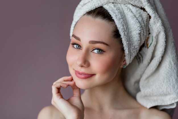 uśmiechnięta młoda kobieta ubrana w szlafrok i ręcznik na głowie, stojąca na różowo