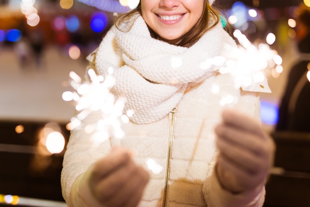 Uśmiechnięta młoda kobieta ubrana w zimowe ubrania z dzianiny, trzymająca brylant na zewnątrz na tle śniegu