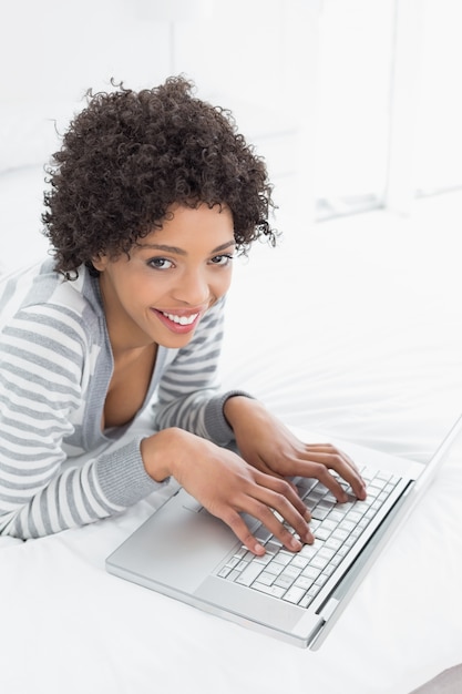 Uśmiechnięta młoda kobieta używa laptop w łóżku
