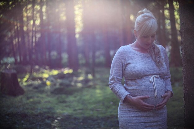 Zdjęcie uśmiechnięta młoda kobieta w ciąży stojąca w lesie