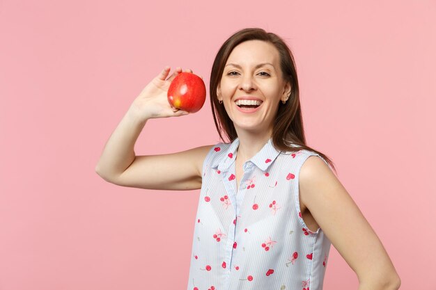 Uśmiechnięta młoda kobieta w letnie ubrania trzymając owoce świeże dojrzałe czerwone jabłko na białym tle na tle różowy pastelowe ściany, portret studio. Żywy styl życia ludzi, koncepcja relaksu wakacje. Makieta miejsca na kopię.