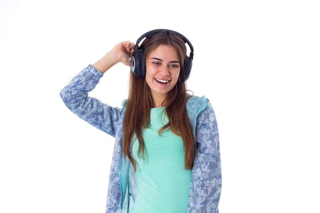 Uśmiechnięta młoda kobieta w niebieskiej koszuli słucha muzyki w czarnych słuchawkach w studio