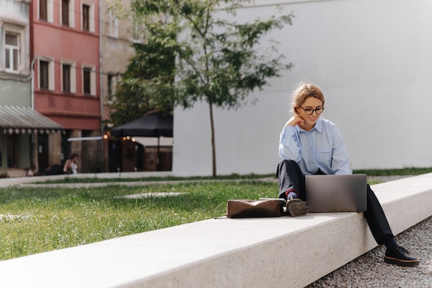 Zdjęcie uśmiechnięta młoda kobieta w odzieży casual i okulary relaks na świeżym powietrzu i przy użyciu komputera przenośnego. konsumpcja ludzi i technologii.