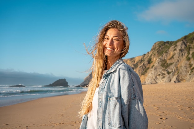 Uśmiechnięta młoda kobieta z długimi blond włosami na letnich wakacjach na plaży