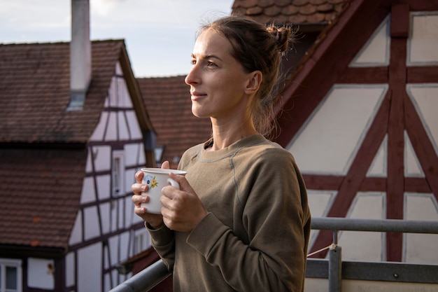 Uśmiechnięta młoda kobieta z filiżanką kawy na tarasie