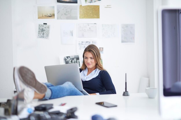 Uśmiechnięta młoda kobieta za pomocą laptopa przy biurku w biurze