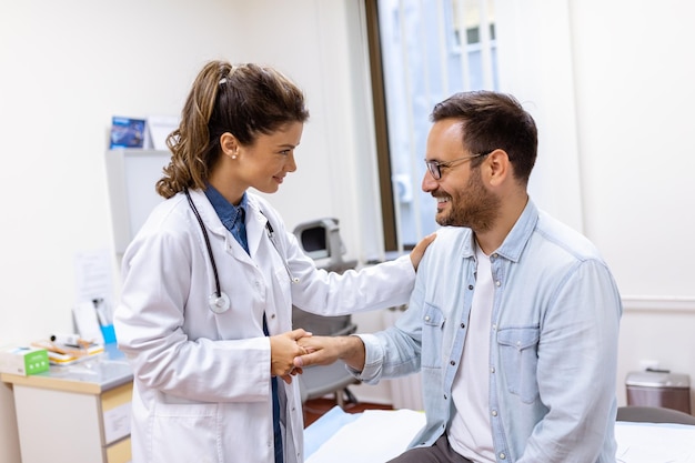 Uśmiechnięta młoda lekarka uścisnąć dłoń zamknij umowę ubezpieczenia zdrowotnego ze starszym pacjentem podczas konsultacji w szpitalu Szczęśliwa kobieta Pozdrowienie lekarza GP zapoznaj się z mężczyzną w klinice