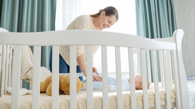 Uśmiechnięta młoda matka z synkiem leżącym rano w kołysce Koncepcja rodzicielskiego szczęścia rodzinnego i rozwoju dziecka