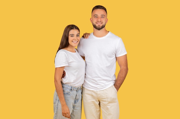 Uśmiechnięta młoda para stoi blisko siebie w zwykłych ubraniach na żółtym tle