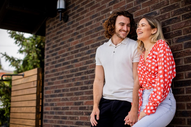 Uśmiechnięta młoda para zakochanych stojących przed murem domu
