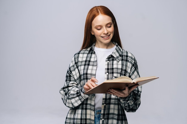 Uśmiechnięta młoda studentka college'u przewraca strony książki podczas czytania