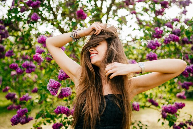 uśmiechnięta modelka z długimi włosami w letnim ogrodzie liliowym