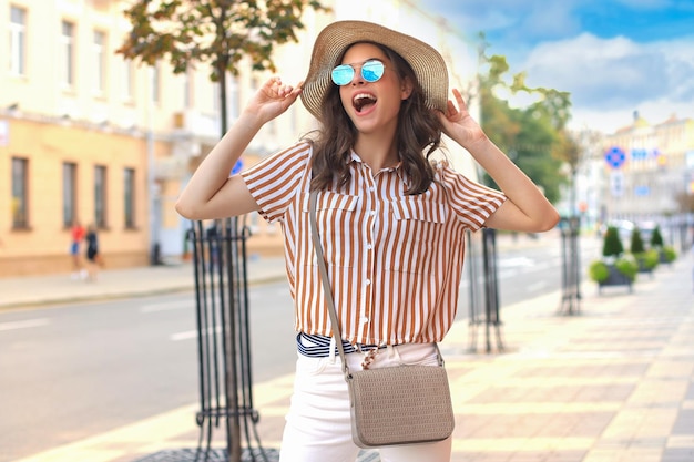 Uśmiechnięta modna dziewczyna hipster pozuje w letnim kapeluszu miejskim