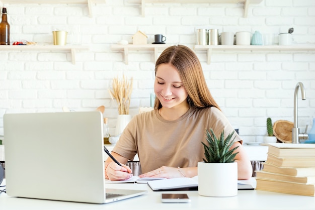 Uśmiechnięta nastolatka płci żeńskiej studiuje na laptopie w domu