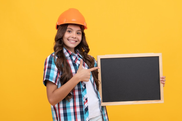 Uśmiechnięta nastoletnia dziewczyna robotnik wskazujący palcem na tablicy reklama dziecka święto pracy