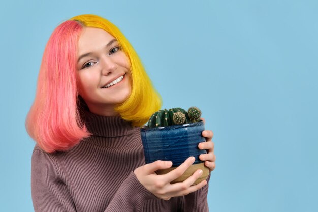 Uśmiechnięta nastoletnia dziewczyna strzał z głowy z farbowanymi włosami, trzymająca garnek z kaktusem