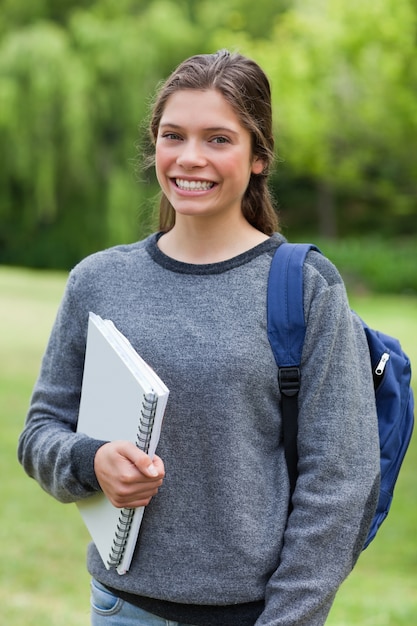 Uśmiechnięta nastoletnia dziewczyna trzyma notatnika podczas gdy stojący w parku