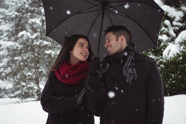 Uśmiechnięta Para Pod Parasolem Stojący W Lesie Podczas Opadów śniegu