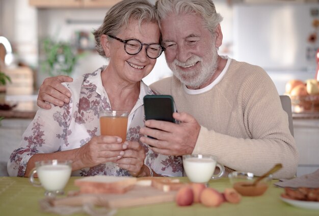 Uśmiechnięta Para Seniorów Patrząca Na Telefon Komórkowy Podczas śniadania W Domu