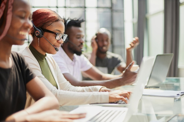 Uśmiechnięta piękna amerykanin afrykańskiego pochodzenia kobieta pracuje w centrum telefonicznym z różnorodną drużyną