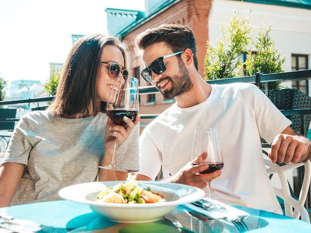 Uśmiechnięta piękna kobieta i jej przystojny chłopak Szczęśliwa wesoła rodzina Para dopingująca kieliszkami czerwonego wina na ich randce w restauracji Piją alkohol na werandzie kawiarni na ulicy