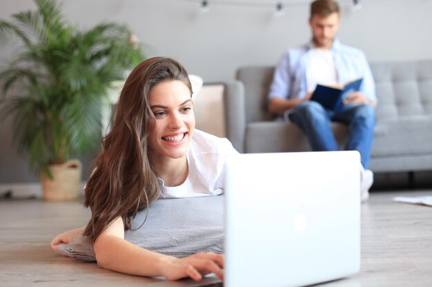 Uśmiechnięta piękna kobieta za pomocą laptopa z zamazanym mężczyzną w tle w domu.