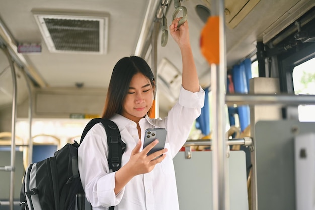 Uśmiechnięta podróżna z plecakiem stojąca w autobusie i korzystająca z telefonu komórkowego Koncepcja podróży i transportu