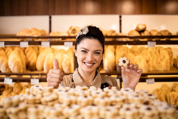 uśmiechnięta pracownica piekarni trzymająca świeżo upieczone ciasteczka w piekarni lub cukierni