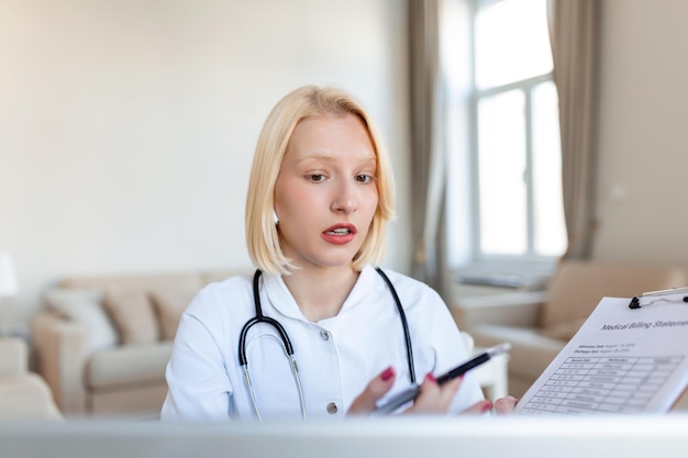 Uśmiechnięta profesjonalna lekarka w mundurze, robiąca notatki w dzienniku medycznym, wypełniająca dokumenty, historia choroby pacjenta, patrząca na ekran laptopa, studentka oglądająca webinarium