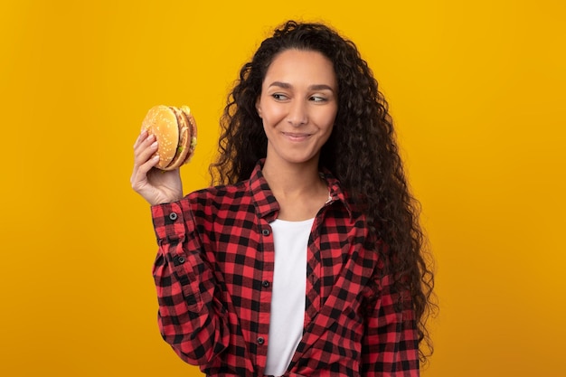 Uśmiechnięta przypadkowa dama trzymająca burgera w studio
