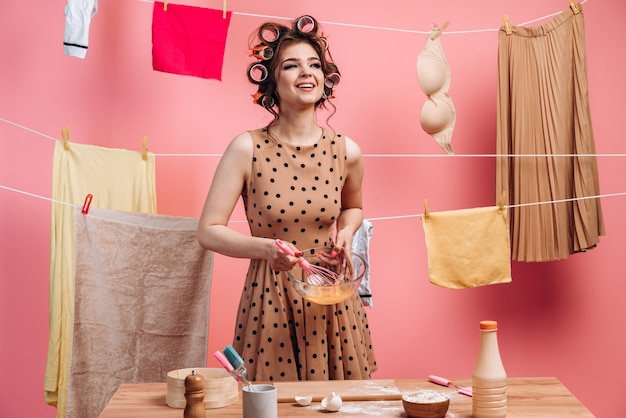 Uśmiechnięta, radosna dziewczyna w sukience w kropki, bijąca jajka, gotująca na tle sznura z ubraniami.