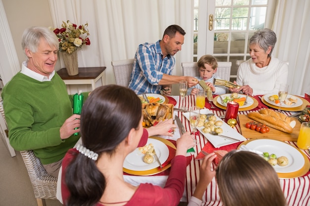 Uśmiechnięta rodzina ciągnie boże narodzenie krakersa przy obiadowym stołem