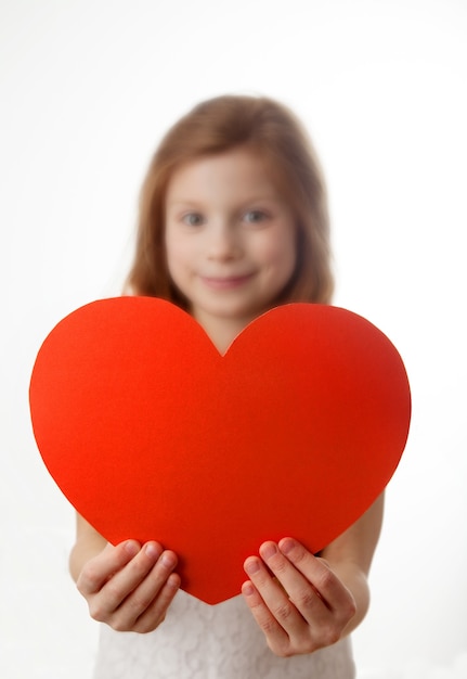 Zdjęcie uśmiechnięta rudowłosa dziewczynka trzyma duże czerwone serce w jej rękach na białym tle