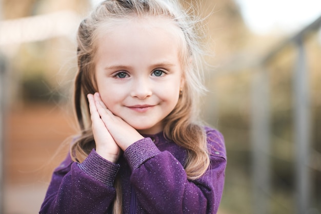 Uśmiechnięta śliczna blond dziewczynka pozuje na zewnątrz nad miastem w parku