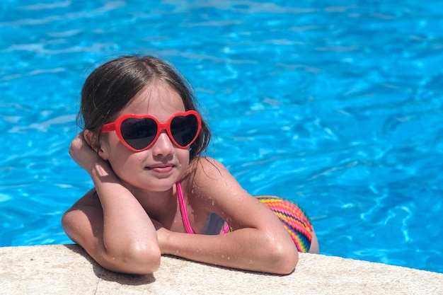 Uśmiechnięta śliczna dziewczynka w okularach przeciwsłonecznych w basenie w słoneczny dzień Dzieciństwo i letnia radość