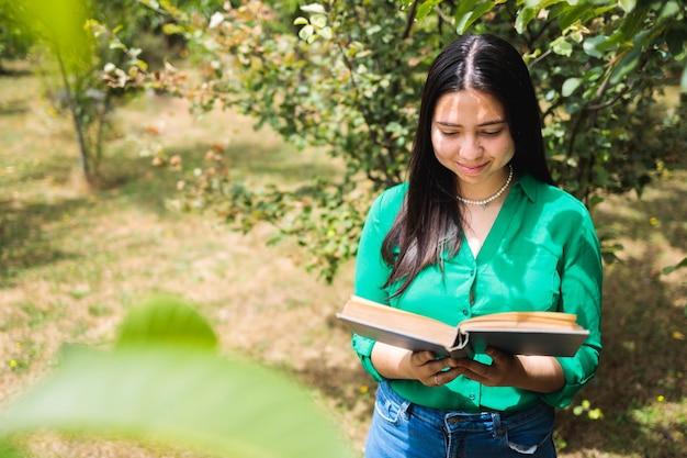 Uśmiechnięta spokojna młoda kobieta czytająca książkę w zieleni pola. Światowy dzień książki. Skopiuj miejsce
