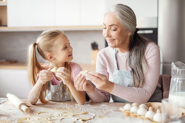 Uśmiechnięta stara babcia w fartuchu uczy małą wnuczkę robienie ciasta formy ciasteczka przygotowują jedzenie