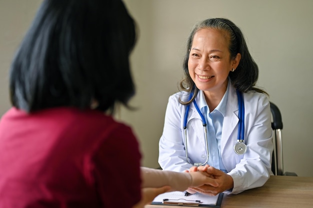 Uśmiechnięta starsza azjatycka lekarka ortopedyczna konsultująca nowy plan leczenia z pacjentem
