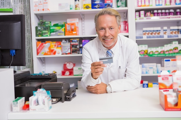 Uśmiechnięta starsza farmaceuta trzyma kredytową kartę