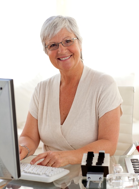 Uśmiechnięta starsza kobieta pracuje z komputerem