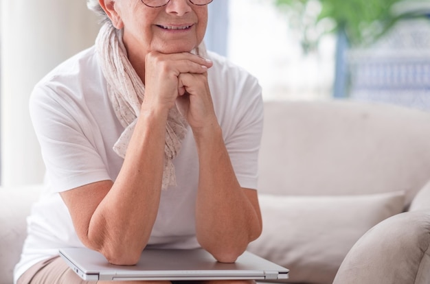 Uśmiechnięta starsza kobieta siedząca na kanapie skończyła pracę i opiera łokcie na laptopie