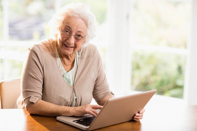 Uśmiechnięta starsza kobieta używa laptop w domu