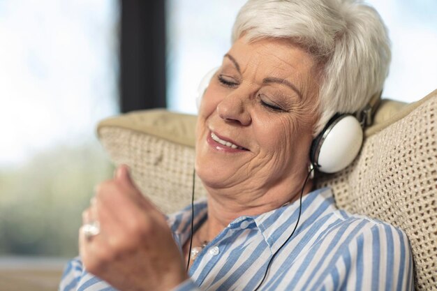 Uśmiechnięta starsza kobieta w słuchawkach słuchająca muzyki w domu