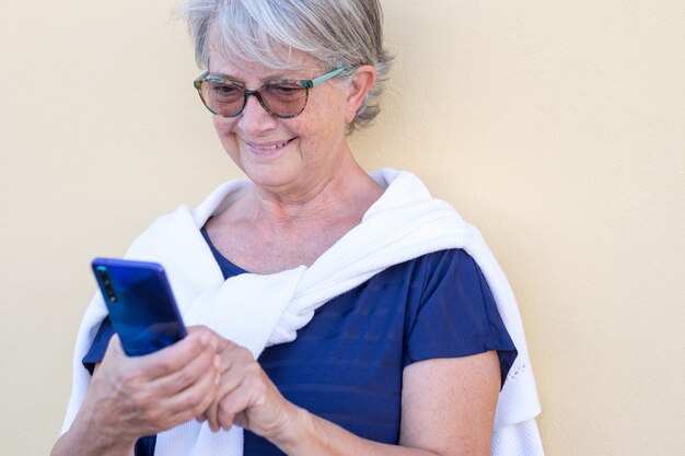 Uśmiechnięta starsza kobieta z białymi włosami przy użyciu telefonu komórkowego w rozmowie wideo. Atrakcyjni emeryci na świeżym powietrzu korzystający z technologii i społeczności