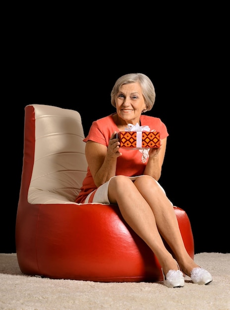 Uśmiechnięta starsza kobieta z prezentem na wypchanym krześle