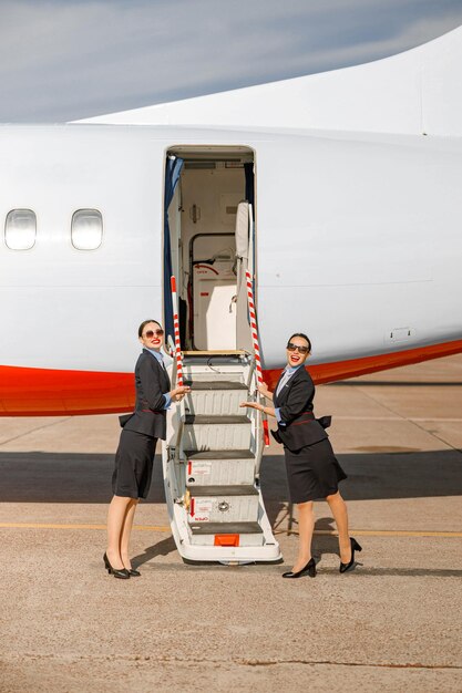 Zdjęcie uśmiechnięta stewardessa stojąca w pobliżu samolotu i zapraszająca na pokład